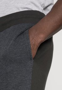 Träningsbyxor i en blandad tygkvalitet. Mörkgrå huvuddela, kolgrå sidopaneler och synlig handficka. Mjuk, strukturerad yta.