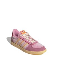 Basket basse dans des tons de rose avec une semelle beige, des lacets blancs, un détail latéral rayé et une étiquette orange avec un motif floral.