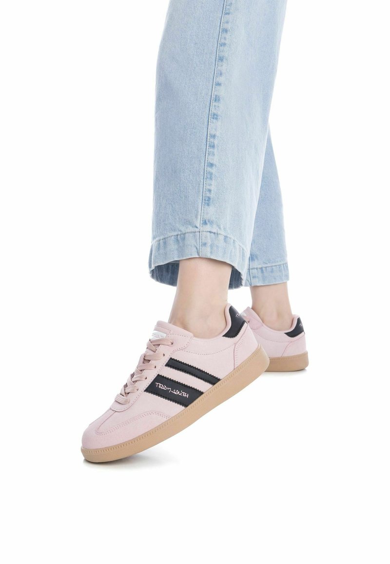 Zapatillas de deporte rosa claro con acentos negros, material de ante, puntera redonda, suela de goma plana y rayas en contraste en los lados.