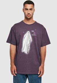 Lila Baumwoll-T-Shirt mit einem weißen Gespenst-Grafik und schwarzen Augen, begleitet von dem Text "Boo und Sachen..." in verspielter Schrift.