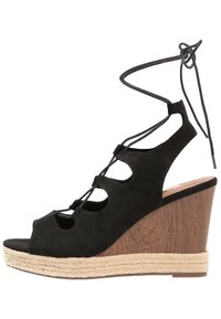 Sandalo a cuneo in suede nero con design peep-toe, caratterizzato da lacci, dettagli intagliati e un tacco a cuneo avvolto in juta con accenti in legno.