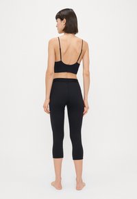 Top desportivo preto com tiras finas e leggings capri pretas de cintura alta. Textura suave, detalhes mínimos e um design ajustado.