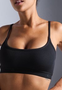Svart ribbet bralette med tynne stropper og bredt bånd. Har en glatt tekstur og minimalistisk design, som vektlegger komfort og passform.