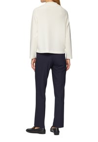 Haut blanc à manches longues avec un col rond, associé à un pantalon bleu marine foncé et des chaussures noires, vu de dos.