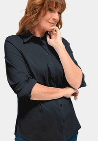 Dark blue button-up shirt with two front pockets, rolled sleeves, and a smooth texture. Fabric appears lightweight and breathable.