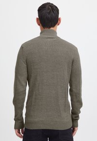 Olivgrüner gestrickter Pullover mit hohem Kragen, langen Ärmeln, gerippten Säumen und strukturierten Details entlang der Schultern und Seiten.