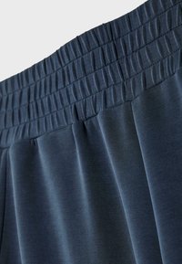 Ceinture élastique bleu foncé sur un pantalon en tissu doux montrant des détails froncés et cousus.