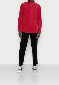 Camisa de button-up de pana roja con cuello, combinada con pantalones de pana negros y zapatillas de lona en blanco y negro.