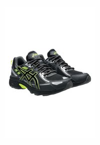 Chaussures de sport noires avec des accents vert fluo, des panneaux en maille et des détails réfléchissants. Elles disposent d'une semelle rembourrée avec des éléments de design angulaires.