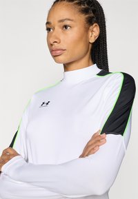 White long-sleeve athletic top with black shoulder panels and neon green accent lines; smooth texture with embroidered logo on the chest.