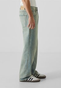 Světle modré džínové kalhoty se rovnými nohavicemi, jemným vyblednutím a štítkem na pase, doplněné černobílými proužkovanými botami.