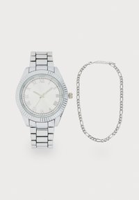 Montre-bracelet argentée avec un cadran rond, des chiffres romains, une lunette striée et un bracelet à maillons. Accompagnée d'un bracelet en chaîne argenté.