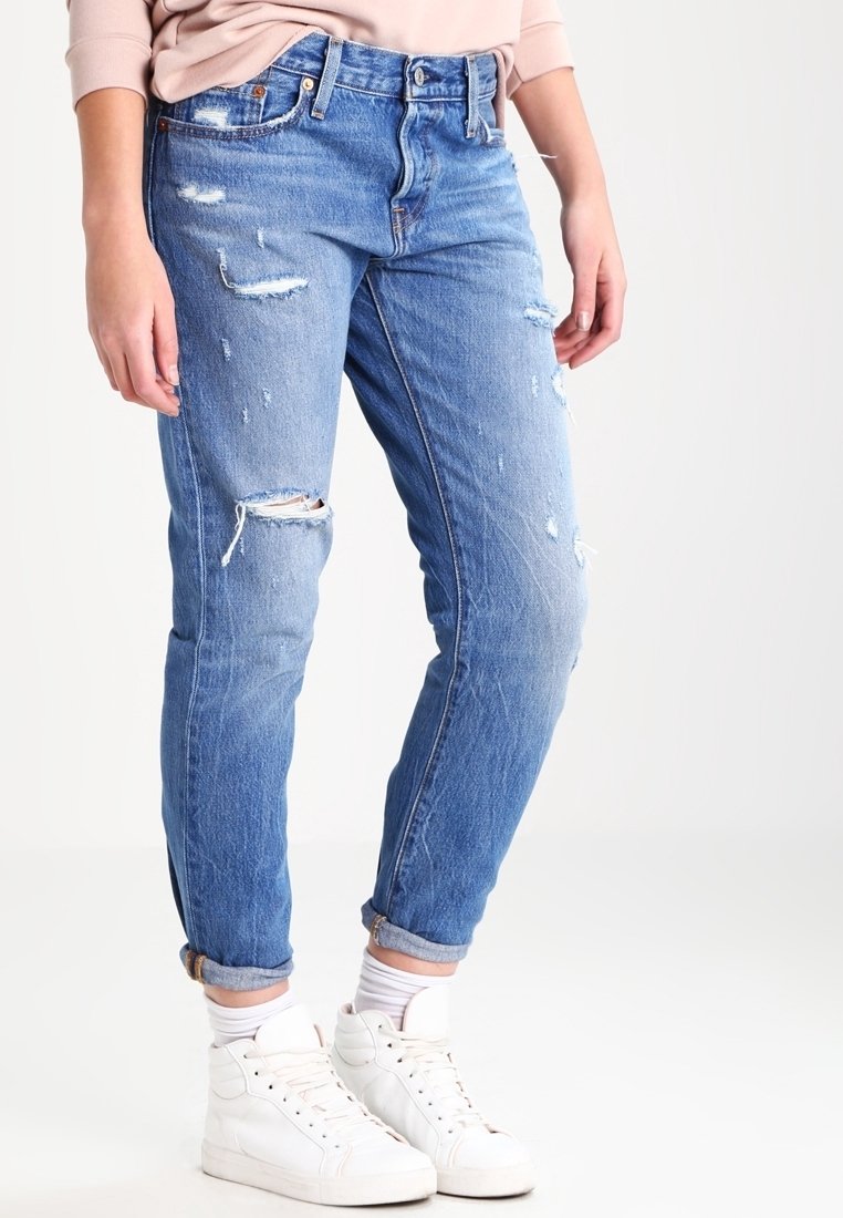 Světle modré džíny z odrbané džínoviny s volným střihem, s roztrženými detaily a ohrnutými nohavicemi, doplněné bílými vysokými teniskami.