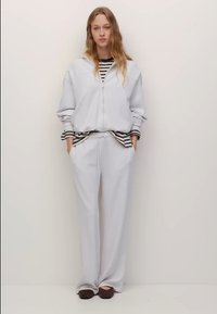 Svetlo siva jopa z zadrgo, kombinirana z ohlapnimi sivimi hlačami. Pod njo je vidna črno-bela črtasta majica. Enostavna zasnova.