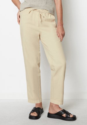 Beige Baumwollhose mit Kordelzug in lockerer Passform und Knöchellänge, kombiniert mit schwarzen Riemchensandalen.