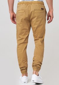 Pantalones jogger beige hechos de tela suave, con una cintura elástica, dobladillos ajustados y dos bolsillos traseros. Combinados con zapatillas blancas.