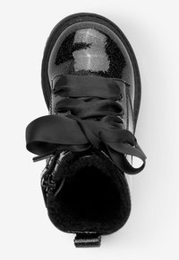 Musta patenttimuovi nilkkaboots glossy-pinnalla, hopeiset glitter-yksityiskohdat, ylisuuret mustat satiininyörit ja pehmeä sisus.