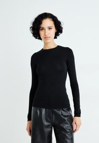 Zwarte lange mouwen top gemaakt van een rekbare stof, met een ronde hals en een aansluitend ontwerp. Gepaard met losse zwarte leren broek.