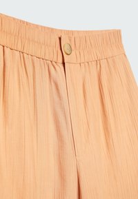 Pleated persikanvärinen kangashame, jossa kuminauhavyötärö ja yksittäinen nappisuljenta. Ominaisuuksiin kuuluu pehmeä tekstuuri ja hillitty kiilto.