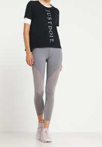 Camiseta negra de mangas cortas con la impresión "JUST DO IT.", combinada con leggins grises que tienen paneles de malla y una silueta ajustada. Zapatillas de deporte rosa claro.