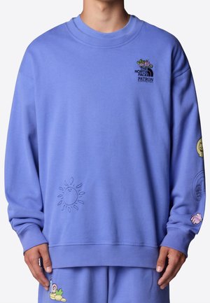 Lavendelfarbener Sweatshirt mit kleiner gestickter Sonne, Blumen, Schnecke und „The North Face Patron“-Logo auf Brust und Ärmel, getragen von einer Person.