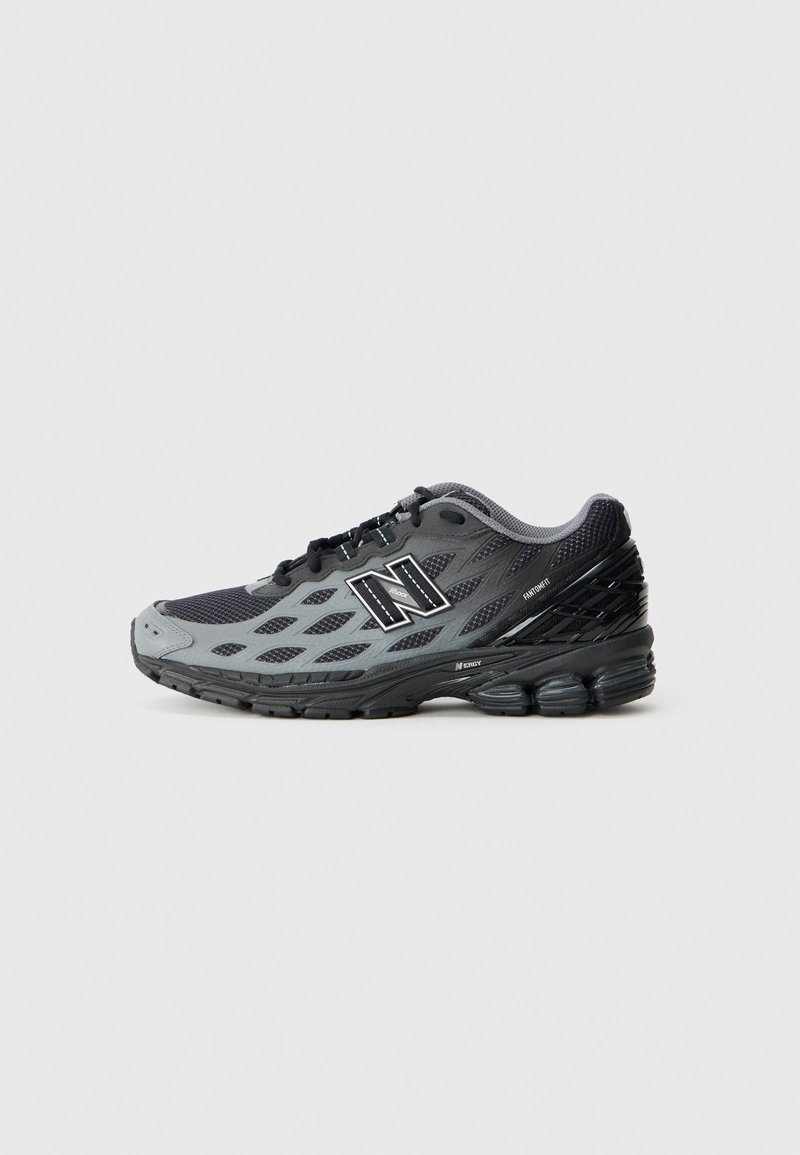 Chaussure de sport New Balance noire et grise avec tige en mesh, semelle rembourrée et lacets noirs, vue de côté sur fond clair.