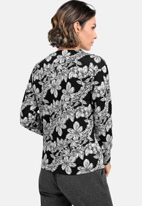 Black long-sleeve top with white floral pattern. Features a round neck and fitted design. Made from a soft, textured fabric.