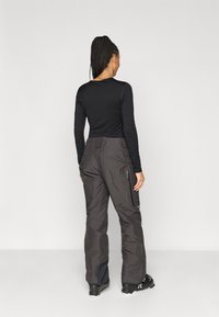 Μαύρη μπλούζα με μακριά μανίκια, συνδυασμένη με γκρι παντελόνια χιονιού που διαθέτουν τσέπες με φερμουάρ, στενές γάμπες και το λογότυπο της Patagonia κοντά στη ζωνη.