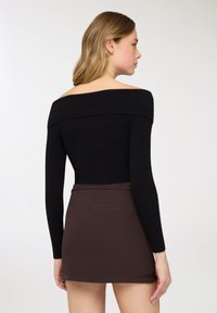 Top nero a coste con scollo a barca e maniche lunghe, abbinato a una mini gonna marrone aderente con una tasca posteriore.