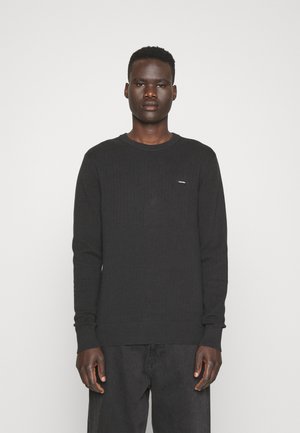 Pullover nero a maniche lunghe con un design a coste testurizzato e scollo rotondo. Presenta un piccolo logo sul petto e polsini aderenti.