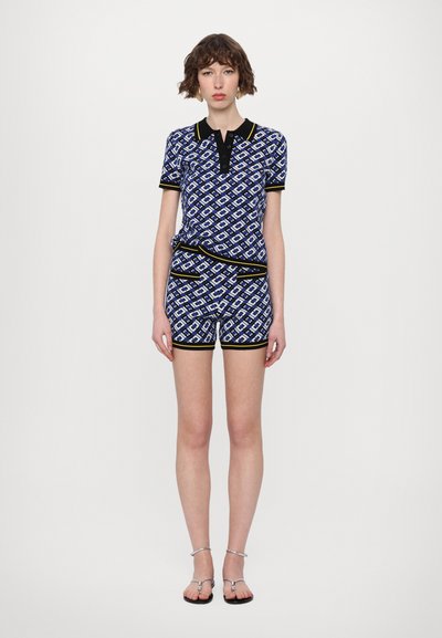 Dvojdílný outfit s modrým geometrickým vzorem, černými detaily, krátkými rukávy a přiléhavým střihem, doplněný o odpovídající šortky.
