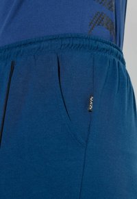 Niebieskie spodnie sportowe wykonane z miękkiego, teksturowanego materiału, z elastyczną talią, boczną kieszenią oraz małą czarną metką "Sports" z przodu.