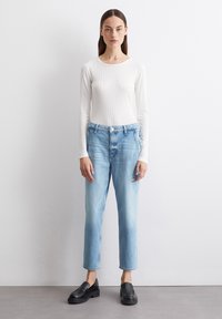 Lett ribbet hvit langermet topp parret med lyseblå rette jeans. Svarte slip-on sko med tykk såle. Ren, minimal design.