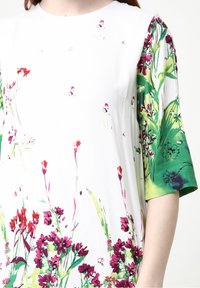 Vestido de manga corta en tela blanca con estampado floral en tonos de rosa y verde. Textura suave con un corte relajado y escote redondo.