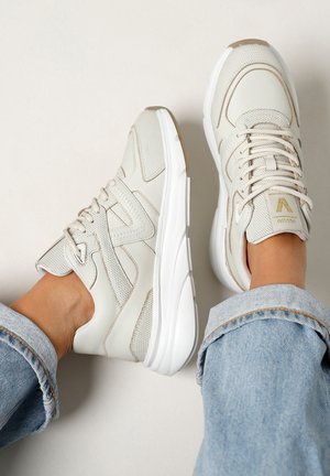 Baskets blanches en cuir avec des accents en maille, dotées d'une semelle épaisse et de détails beige clair. Surfaces texturées et design à lacets visibles.