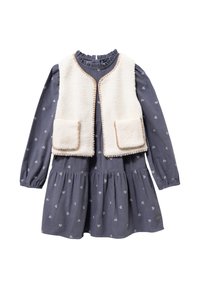 Vestido azul marino con estampado de corazones, mangas largas y falda fruncida, combinado con un chaleco de piel sintética color crema con ribetes marrones y bolsillos.
