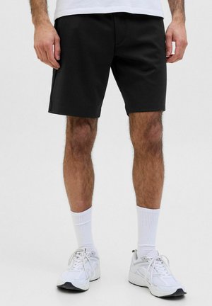 Schwarze Shorts mit elastischem Bund, knielang, aus einem weichen Baumwollgemisch. Kombiniert mit weißen Crew-Socken und Sneakers.