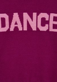 Violet džemperis ar lieliem rozā burtiem, kuros rakstīts "DANCE". Audums izskatās mīksts ar gludu tekstūru. Dizains ir drosmīgs un vienkāršs.