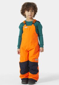 Jasně oranžové nepromokavé kombinézy s námořnickými akcenty, nastavitelnými popruhy a kontrastním logem na hrudi a nohávě.