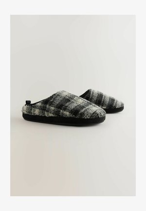 Pantofole a strisce bianche e nere con una texture morbida e pelosa, forma arrotondata e suola in gomma, dotate di un utile manico sul retro.