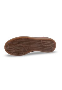 Semelle de chaussure avec un talon en caoutchouc brun présentant un motif en chevrons et des rainures courbes sur un fond blanc.