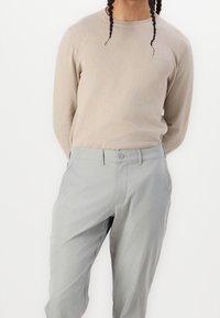 Beige långärmad tröja med rund halsringning kombinerad med ljusgrå byxor med knappstängning och fickor, slät tygstruktur.