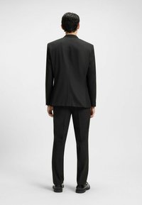 Schwarzer Anzug, taillierte Passform, gerader Schnitt, glattes Gewebe, Rückenansicht, minimale Details, mit schwarzen Schuhen auf einem einfarbigen Hintergrund.
