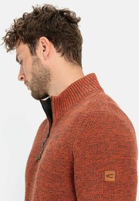 Pullover mit Viertelreißverschluss aus gestricktem Stoff in Orange und Schwarz, mit strukturiertem Muster, geripptem Kragen und Lederakzent am Ärmel. Weicher, warmer Stoff.