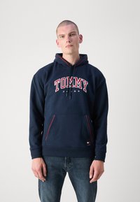 Námornícka mikina s červenobielym logom "TOMMY JEANS". Obsahuje klokanie vrecko a šnúrku s červenými akcentmi. Zloženie z bavlneného mixu.
