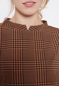 Top i brunt och svart med mönster som har en subtil V-ringning och geometriskt tryck med varierande former och texturer.