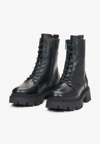Czarne skórzane botki za kostkę z masywną podeszwą, sznurówką z przodu i zamkiem błyskawicznym z boku. Gładka tekstura z surowym wzornictwem i wzmocnionymi akcentami szwów.