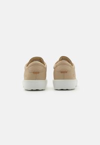 Sneakers in pelle beige con una finitura testurizzata, suole in gomma bianca e design minimalista. Presentano un piccolo tab con logo sul tallone.