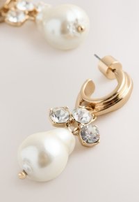 Gold-tone metal earrings featuring a large white faux pearl and three round clear gemstones, showcasing a curved hook design.