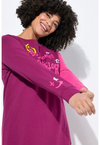 Haut à manches longues en violet et rose avec une coupe décontractée, présentant des graphismes ludiques en jaune et blanc, et des poignets côtelés pour une finition confortable.